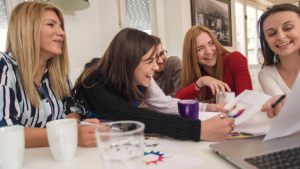 Ett team som samarbetar runt ett bord, skrattar och diskuterar – symbol för ansvar som delas.